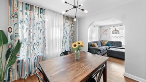 A dining area with a wooden table, chairs, and a vase with sunflowers. There is a sofa and a window with curtains in the background. - Sunny Side Murry Hill Home (Jacksonville)