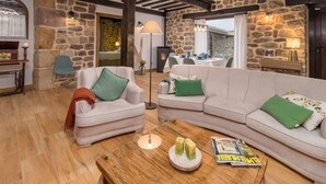 Ein gemütliches Wohnzimmer mit Steinwand, Holzbalken und einem großen Sofa mit grünen Kissen.