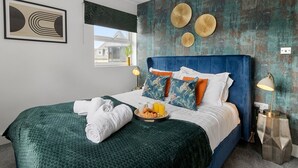 Ett modernt hotellrum med en stor säng, dekorativa kuddar, ett bricka med croissanter och juice samt utsikt över omgivningarna.