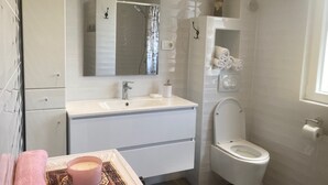 Un baño moderno con tocador blanco, espejo, inodoro y zona de ducha.