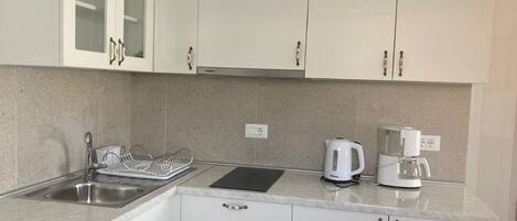 Una cocina con armarios blancos, un lavamanos de acero inoxidable, una tetera y una cafetera.