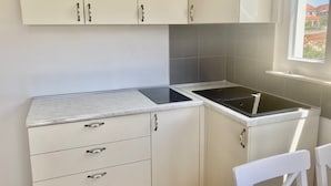 Una cocina con armarios blancos, una placa de inducción negra y una silla blanca.
