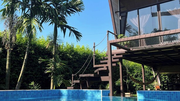 A clear blue pool with a wooden deck and a building with a sign reading 'RUZIC'. - Luxury Glamping in Ruztico (Villavicencio)