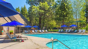 Una piscina con ombrelloni blu, lettini e un edificio con tetto spiovente.
