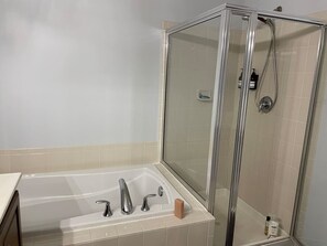 A bathroom with a glass-enclosed shower, a bathtub with two faucets, and a soap dispenser on the wall.