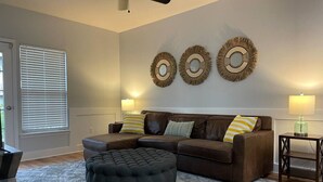 A living room with a brown leather sofa, a round ottoman, and three wall-mounted decorative mirrors.