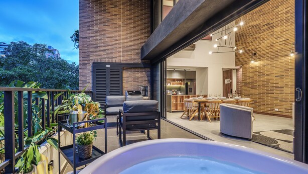 Un espacio exterior moderno con un jacuzzi, asientos y vistas al comedor interior.