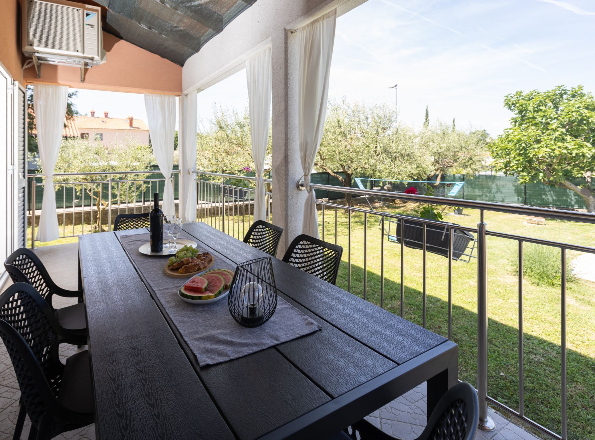A balcony with a table set for dining, featuring a bottle, wine glasses, and a plate of food.