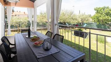 A balcony with a table set for dining, featuring a bottle, wine glasses, and a plate of food.