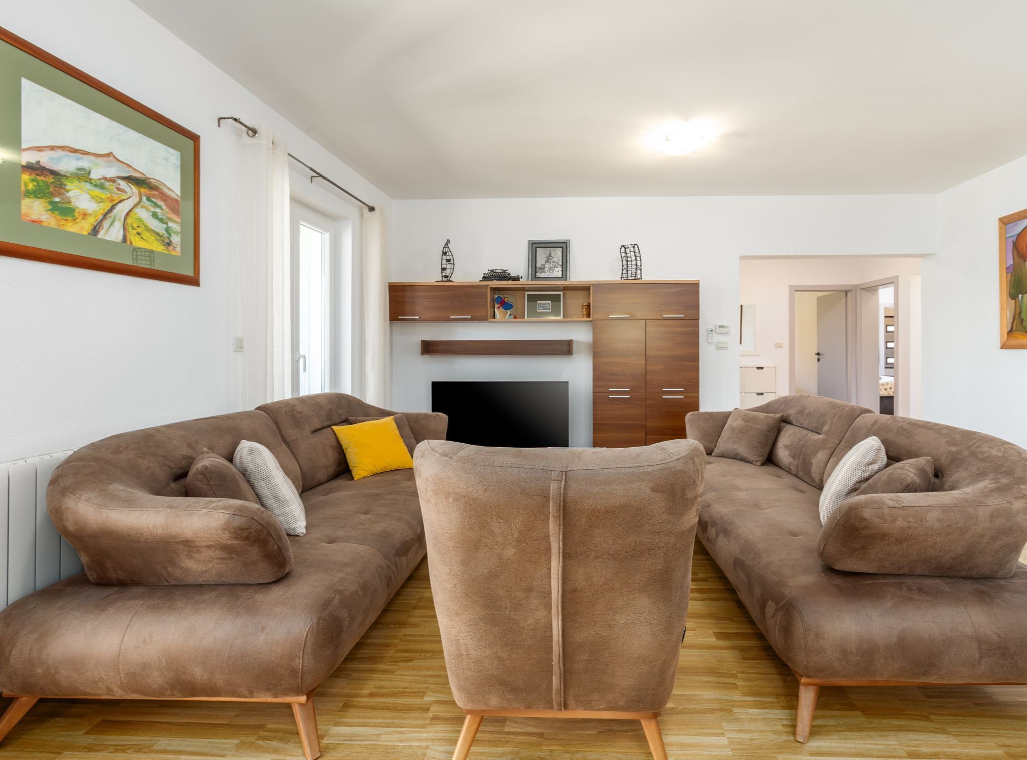 A living room with two brown sofas, a TV, wooden cabinets, and a painting on the wall.