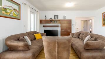 A living room with two brown sofas, a TV, wooden cabinets, and a painting on the wall.