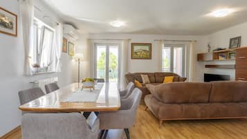 A modern living room with a wooden dining table, grey chairs, a brown sofa, and a TV.