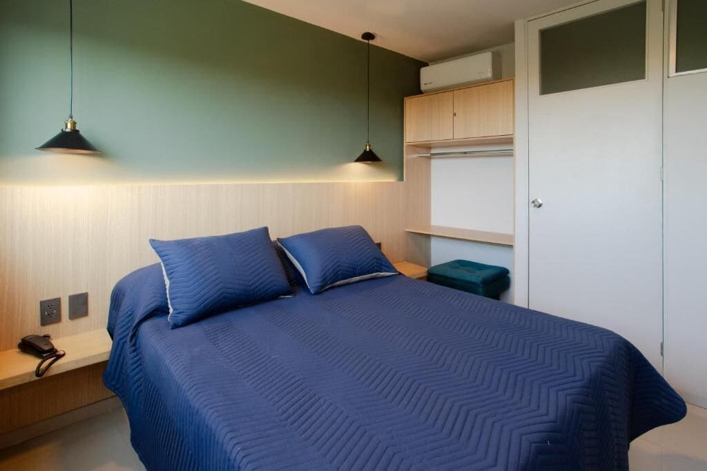 Une chambre à coucher avec un lit, deux lampes de chevet, une table de chevet, un banc vert et une armoire.