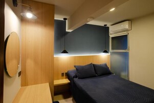 A compact bedroom with a bed, bedside tables, a hanging light fixture, and an air conditioning unit.