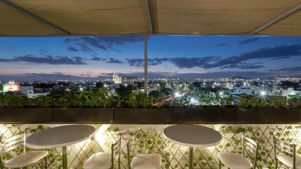 An outdoor seating area with tables and chairs, overlooking a cityscape at dusk. - La Hospedería León (León)