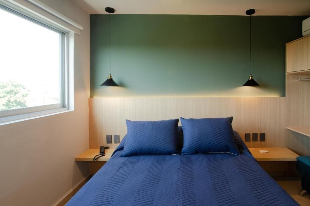 Un dormitorio con una cama, dos mesitas de noche, una mesita auxiliar, una ventana y dos lámparas colgantes.