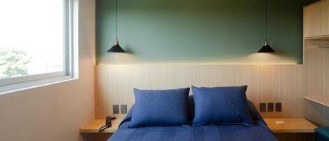 A bedroom with a bed, two bedside tables, a nightstand, a window, and two pendant lights.