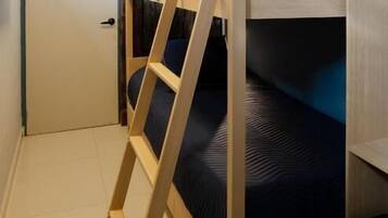 Una cama litera con escalera de madera, colchón azul oscuro y una puerta blanca al fondo.