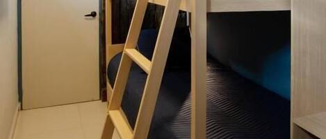 A bunk bed with a wooden ladder, a dark blue mattress, and a white door in the background.