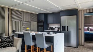 A modern kitchen with a central island, built-in appliances, and a dining area with chairs. - Badgers Sett (Upper Minety)