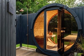 A circular wooden structure with a glass door, a wooden deck, and a small outdoor seating area with a table and chairs. - Badgers Sett (Upper Minety)