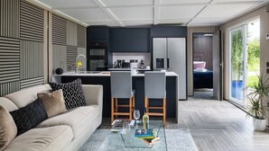 A modern living room with a sofa, coffee table, and a kitchen area with a dining table. - Badgers Sett (Upper Minety)