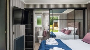 A modern hotel room with a large bed, a TV, and a view of the garden. - Badgers Sett (Upper Minety)