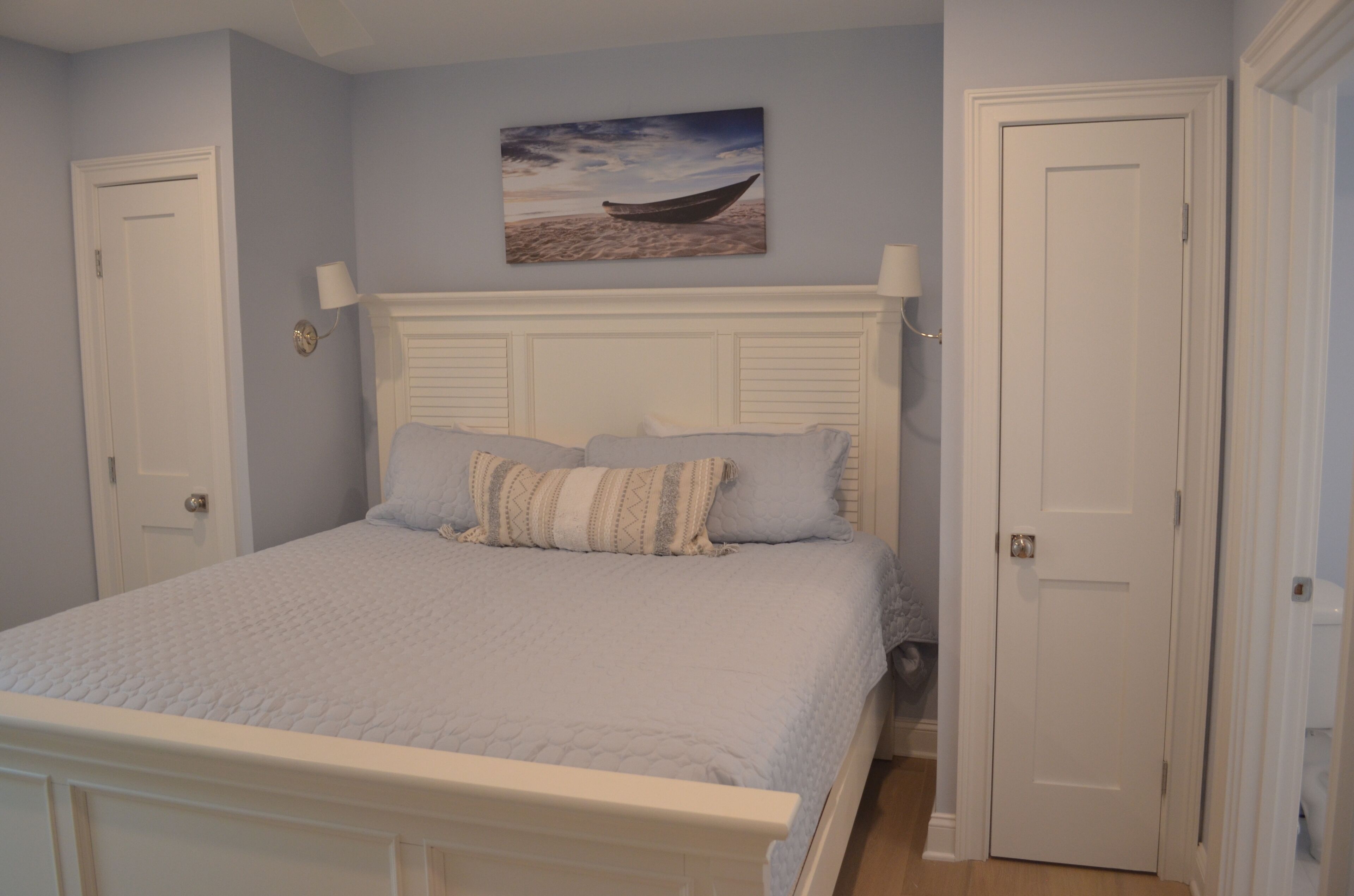 Une chambre à coucher avec un lit, une tête de lit, une lampe fixée au mur et une porte.