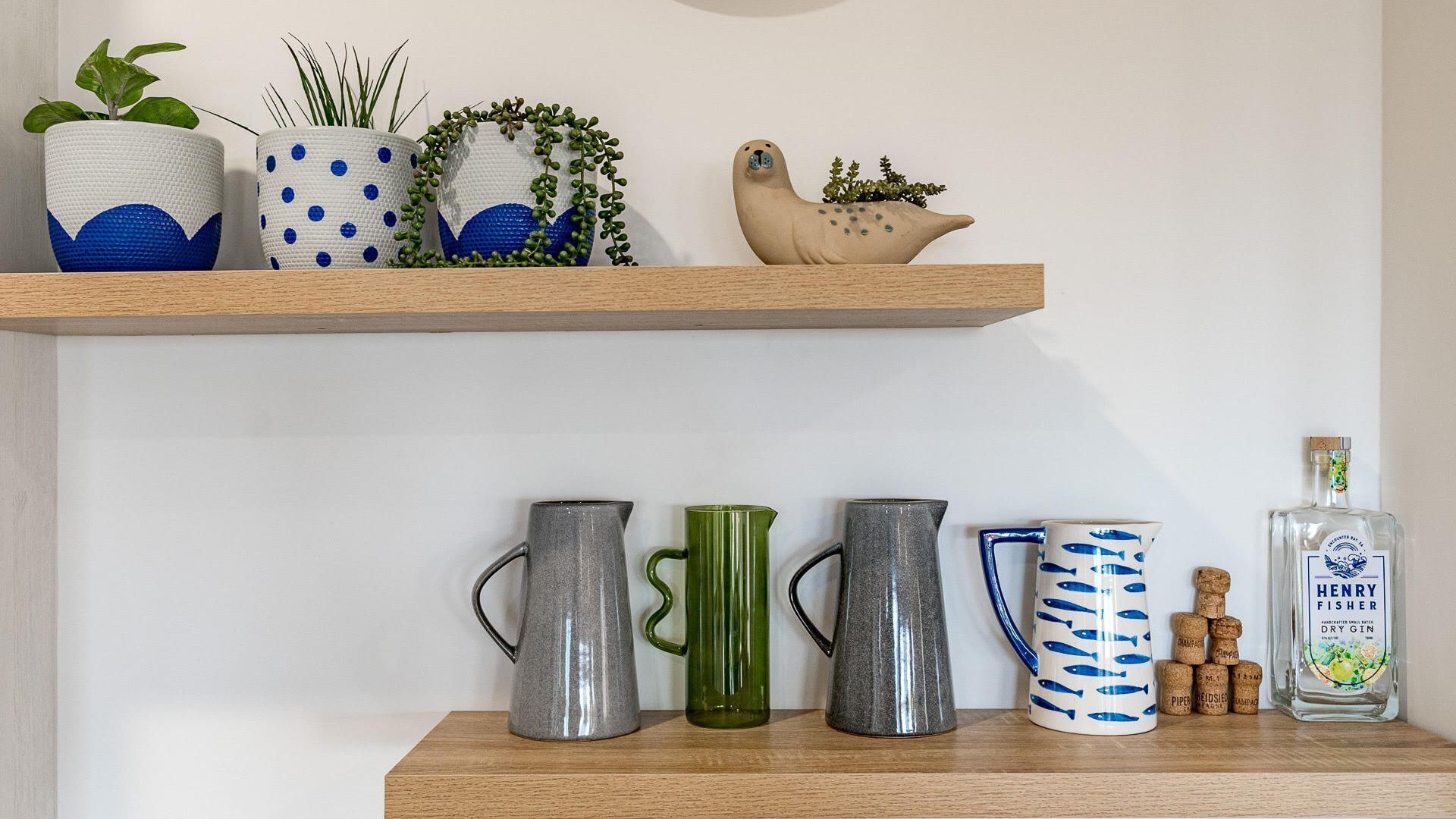 A shelf with various decorative items including potted plants, a ceramic seal, and a bottle of Henry Fisher Dry Gin.