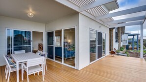 A modern house with a wooden deck, large sliding glass doors, and a dining area with a white table and chairs.