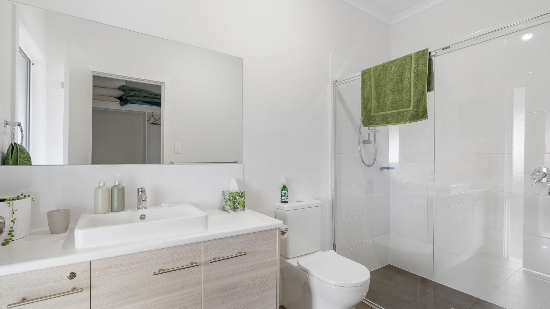 A modern bathroom with a white sink, toilet, and shower. There is a green towel hanging on the shower door.