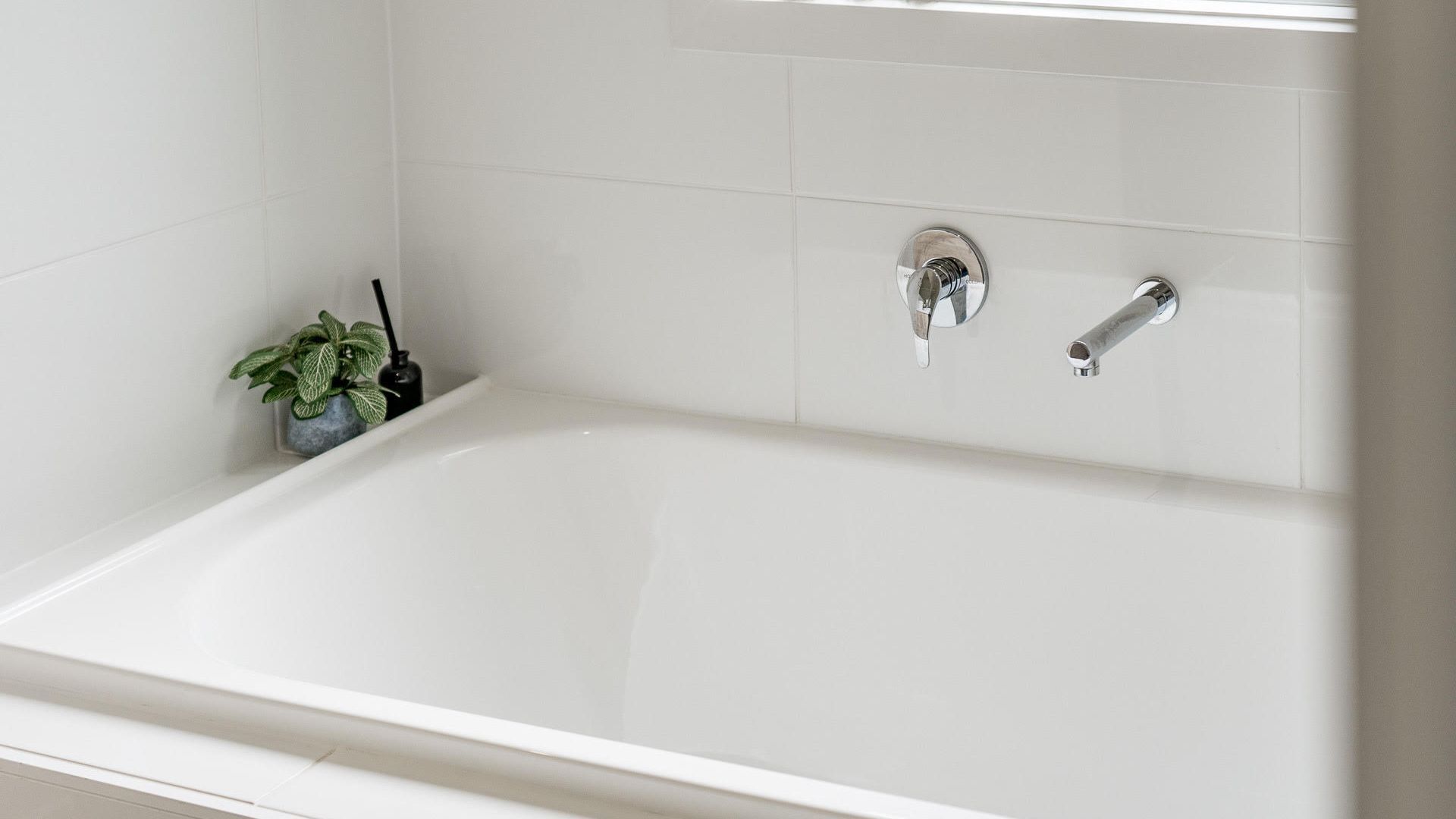 Une salle de bain moderne avec une baignoire blanche, un robinet et une petite plante en pot.