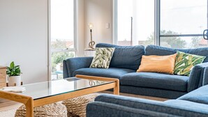 A modern living room with a blue sofa, a glass coffee table, and a potted plant.