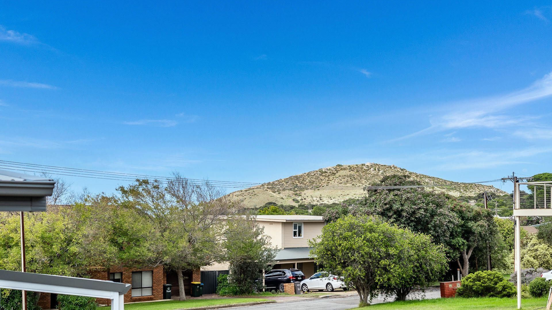 A residential street with houses, parked cars, and a hill in the background.