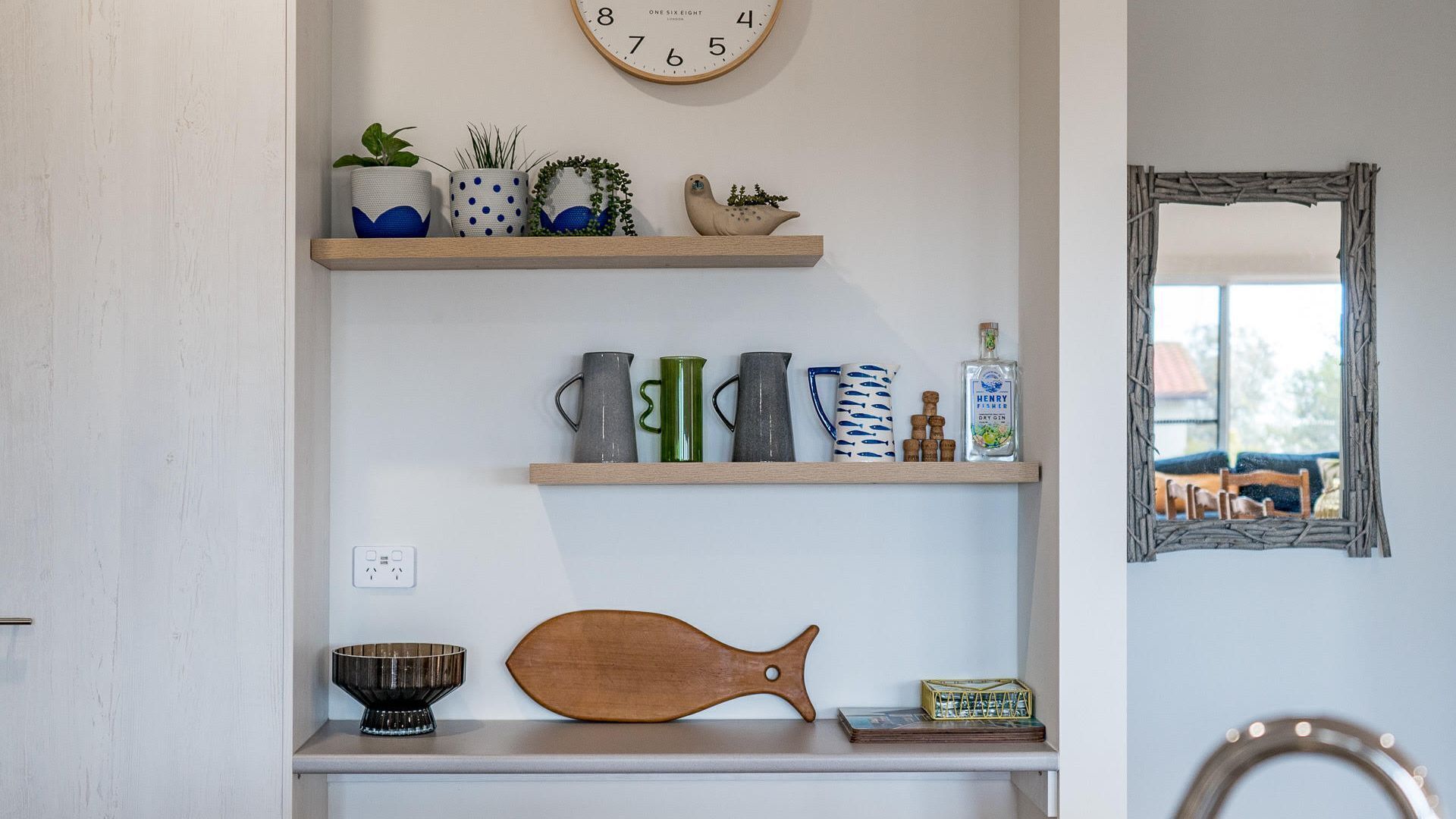 A kitchen with wooden shelves holding various kitchenware, a clock, and a mirror.