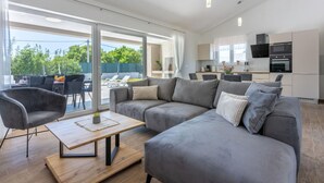 A modern living room with a grey sectional sofa, a wooden coffee table, and a dining area with a table and chairs. - Villa Sabina - Brgod (Rasa)