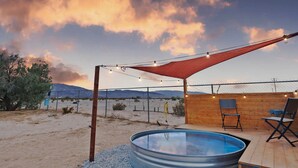 Un área de piscina con terraza de madera, zona de estar cubierta y vistas a las montañas.