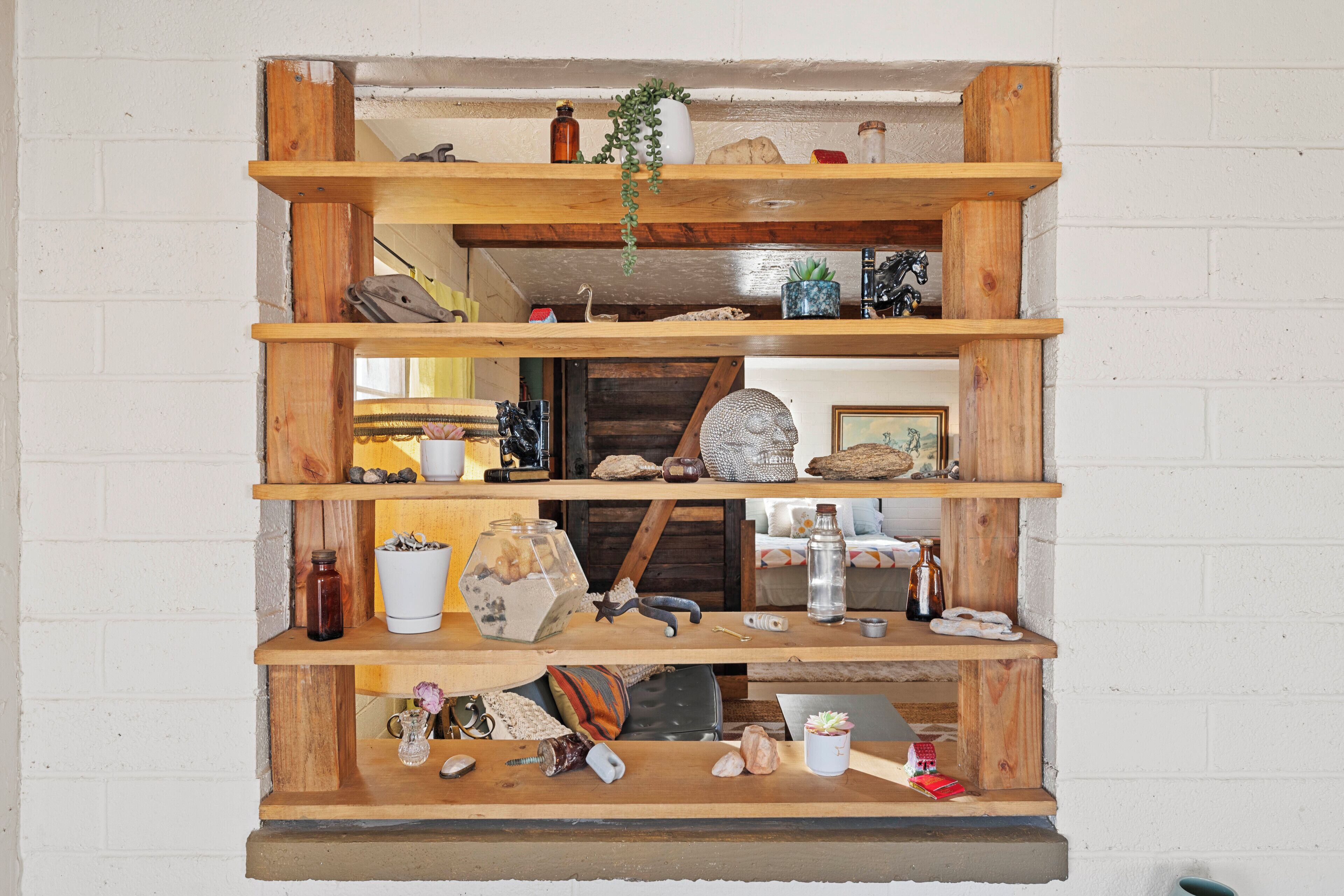 Een houten, meerlaags schap tegen een witte bakstenen muur, met diverse decoratieve items en objecten.