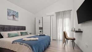Een moderne slaapkamer met een groot bed, een stoel, een televisie en een raam met gordijnen.