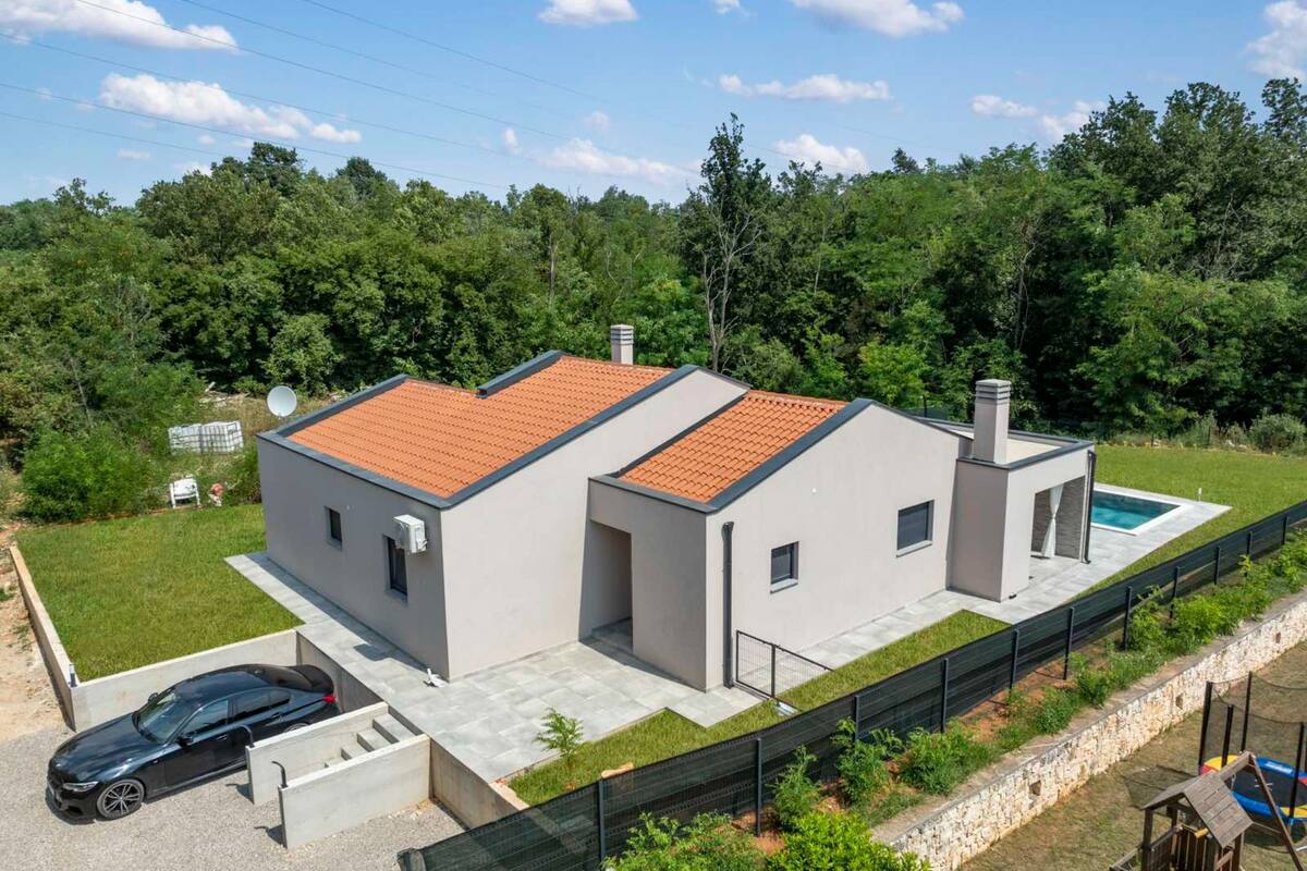Une maison moderne à deux étages, avec un toit en tuiles, une piscine et une cour clôturée.