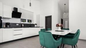 Een moderne keuken met witte kasten, een zwart aanrecht en een eethoek met groene stoelen en een witte tafel.