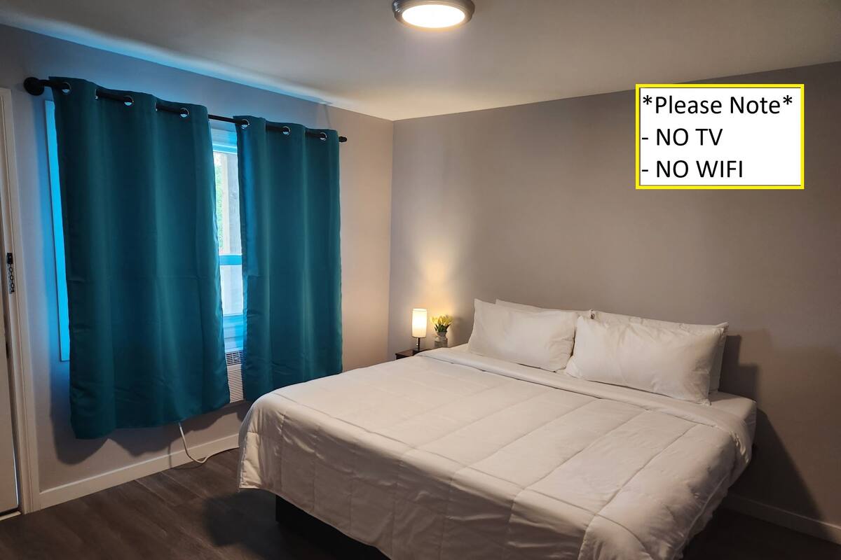 A bedroom with a bed, curtains, a nightstand, and a wall-mounted light. A note indicates no TV or WiFi.