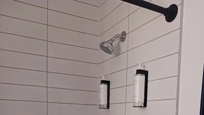 Una doccia con soffione flessibile, rubinetto a muro e due flaconi di shampoo su un portaoggetti nero.