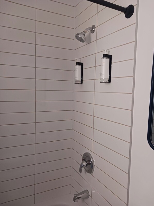 Ducha con cabezal de ducha manual, grifo empotrado en la pared y dos botellas de champú sobre un soporte negro.