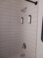 Ducha con cabezal de ducha manual, grifo empotrado en la pared y dos botellas de champú sobre un soporte negro.