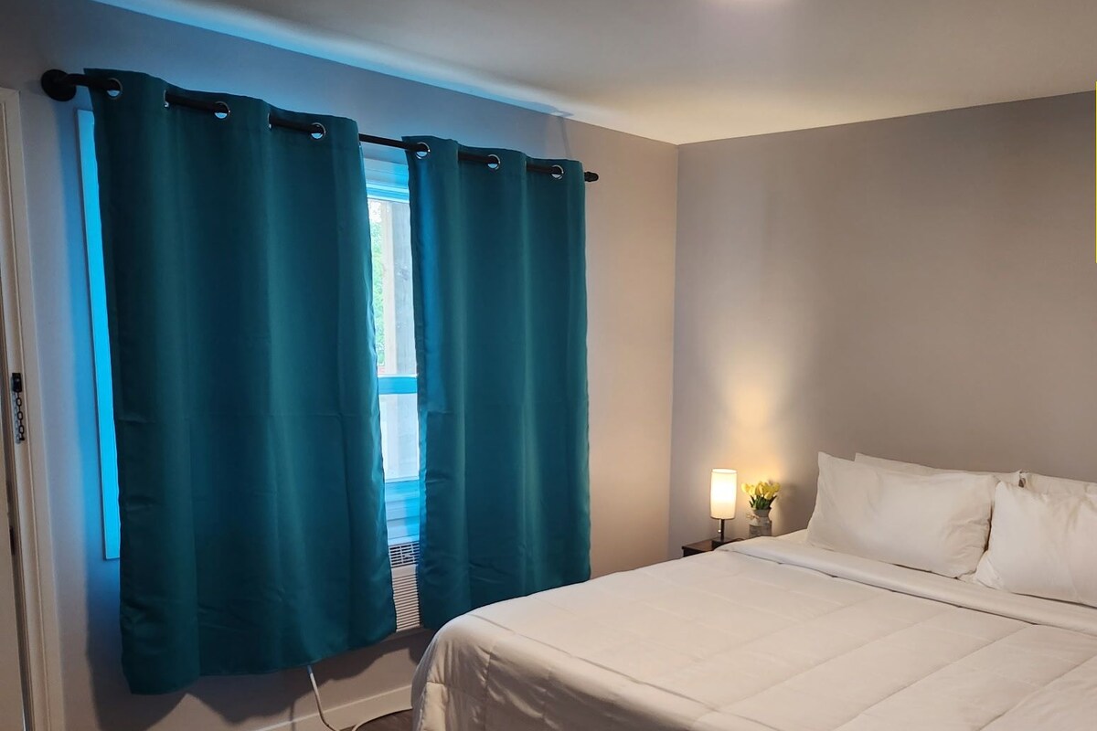 Un dormitorio con cama, cortinas, una mesita de noche y una lámpara de pared. Una nota indica que no hay televisión ni WiFi.