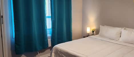 Ein Schlafzimmer mit Bett, Vorhängen, einem Nachttisch und einer Wandleuchte. Ein Hinweis weist darauf hin, dass kein Fernseher oder WLAN vorhanden ist.
