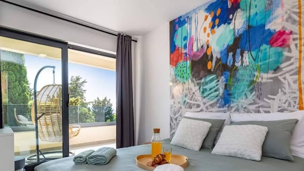 Un dormitorio moderno con una cama grande, un cuadro abstracto de colores y un balcón con una silla colgante.