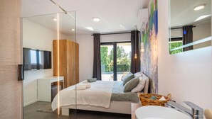 Un dormitorio moderno con una cama grande, cabina de ducha de vidrio, televisor y baño con lavabo y espejo.