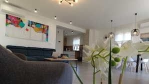 Una sala de estar moderna con un sofá azul, un comedor con sillas blancas y una cocina al fondo.